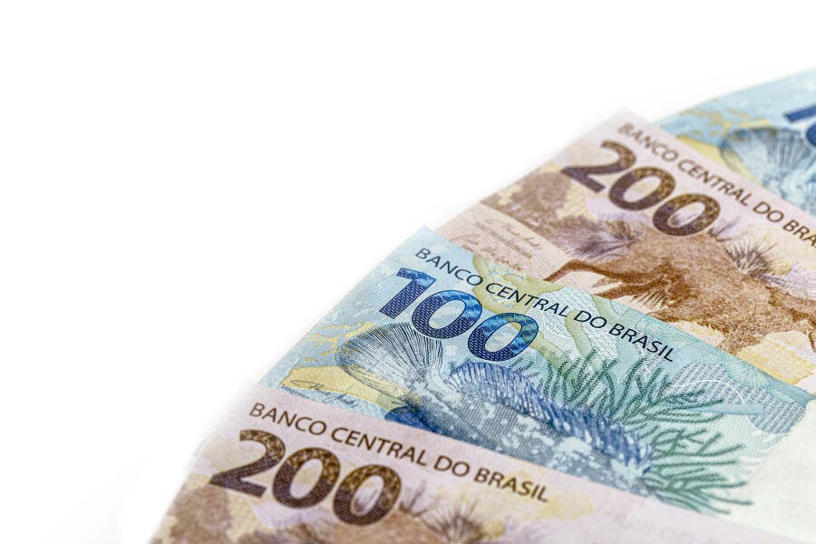 Notas de cem e duzentos reais brasileiros empilhadas em fundo branco