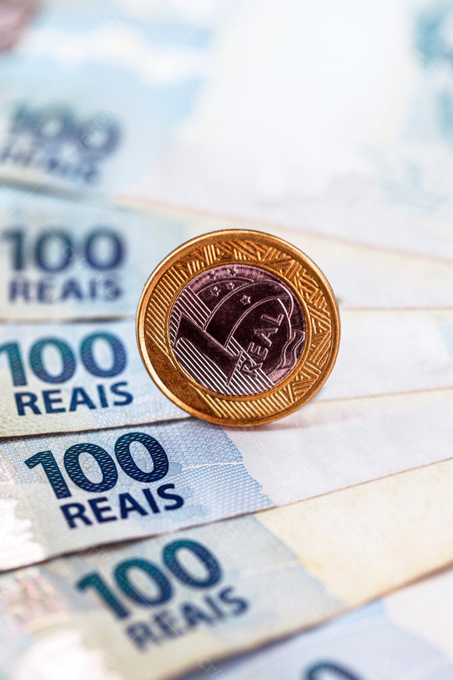 Moeda de um real brasileira em pé sobre notas de cem reais