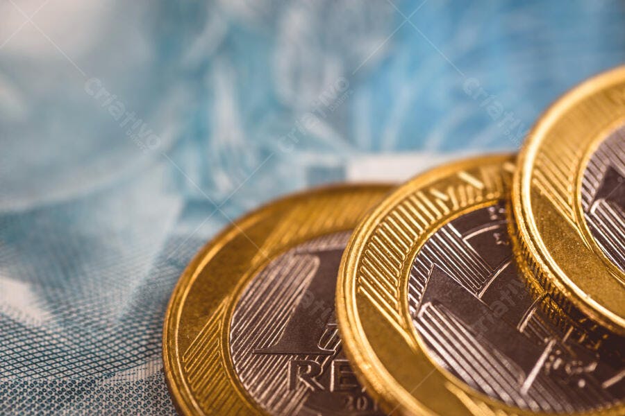 Moedas de real brasileiras empilhadas sobre cédula azul em close-up