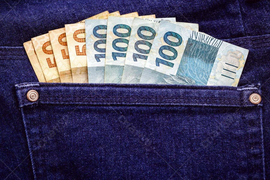 Notas de 50 e 100 reais no bolso da calça jeans azul marinho