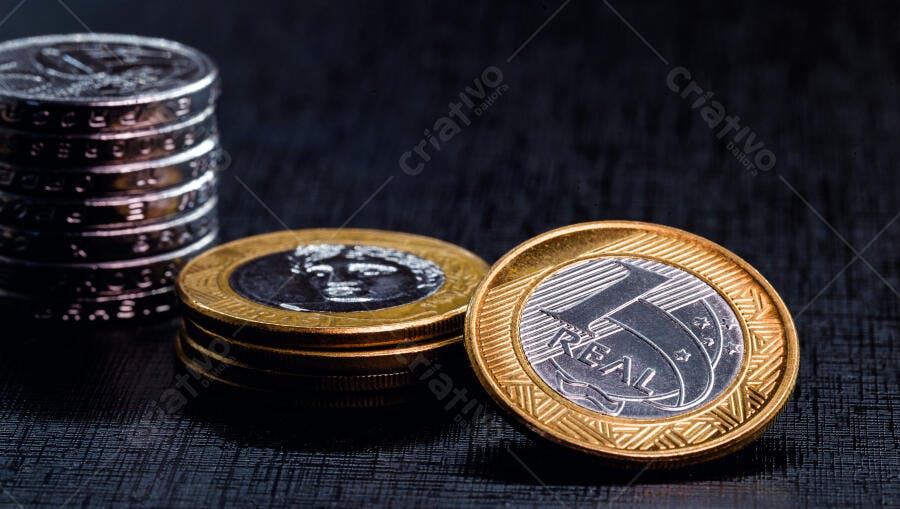 Moedas de Real brasileiro empilhadas sobre fundo escuro