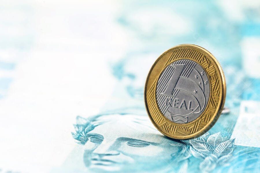 Moeda de 1 Real brasileiro em pé sobre nota de dinheiro azul e branca