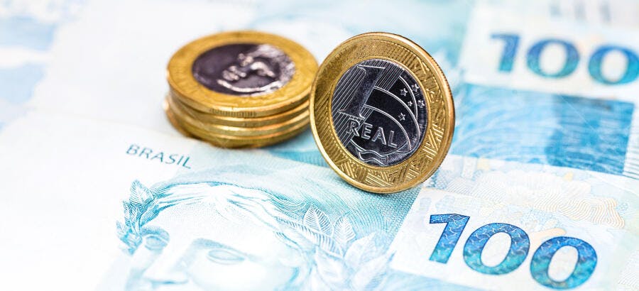 Moedas de Real douradas e prateadas sobre notas azuis de 100 Reais do Brasil