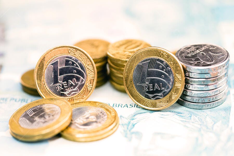 Moedas de real brasileiras prateadas e douradas sobre notas de dinheiro azul