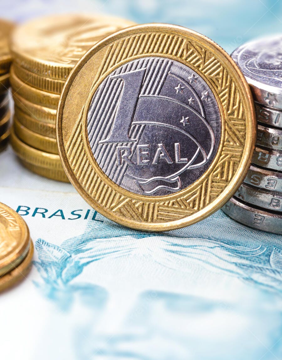 Moeda de um Real dourada e prateada com notas de dinheiro empilhadas