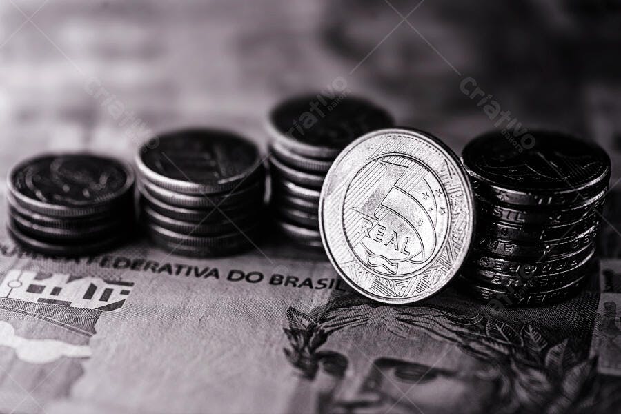 Pilhas de moedas brasileiras e nota de Real em preto e branco economia