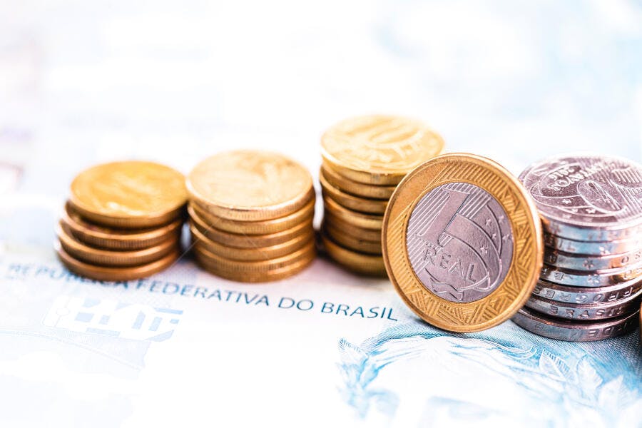 Moedas brasileiras de Real douradas e prateadas empilhadas em notas financeiras