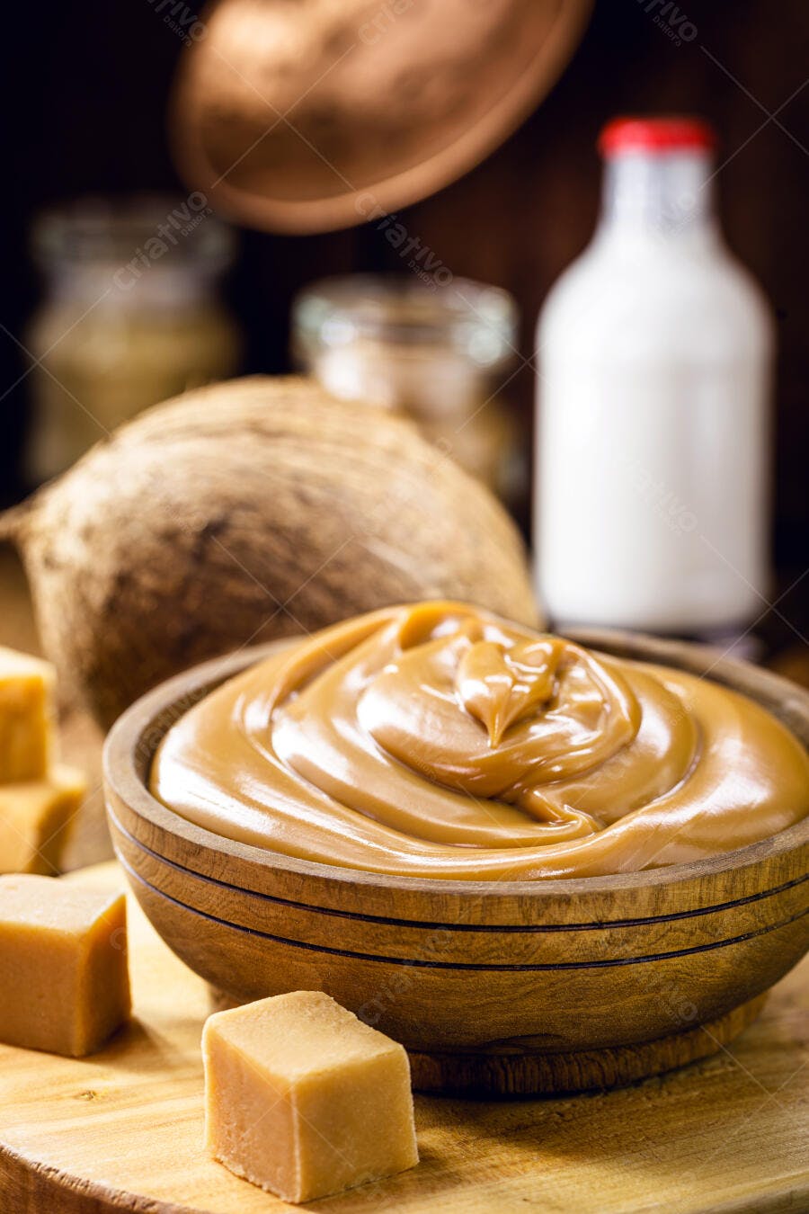 Doce de leite cremoso em tigela de madeira com coco e caramelos