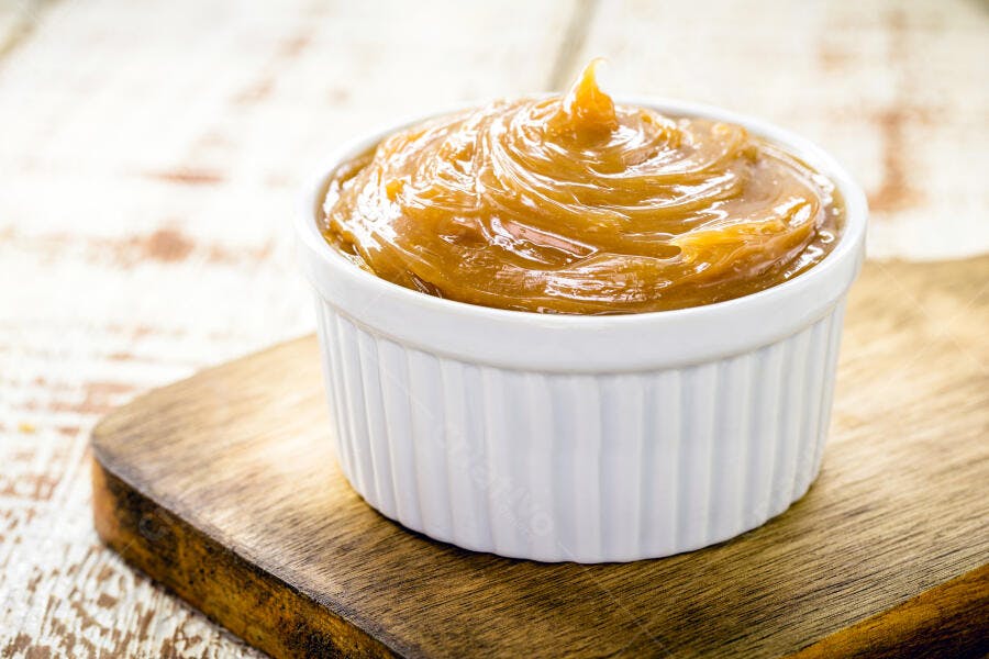 Doce de leite cremoso em tigela branca sobre tábua rústica de madeira