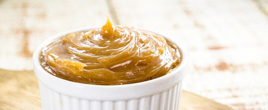 Doce de leite cremoso em pote branco sobre madeira clara