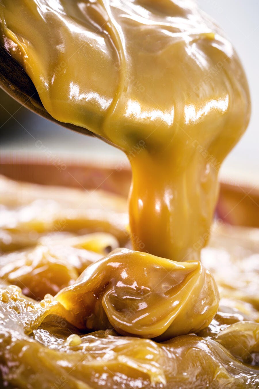Doce de leite cremoso dourado sendo servido com colher de pau
