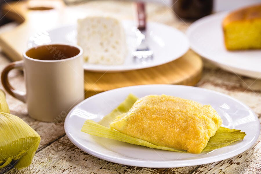 Pamonha amarela tradicional com café e queijo fresco na mesa de madeira rústica