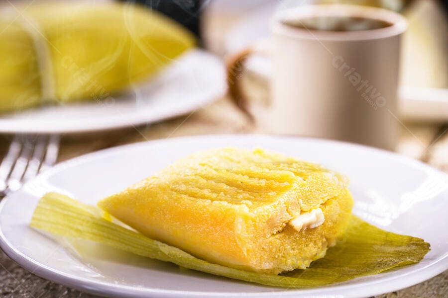 Pamonha de milho amarela com queijo em prato branco rústico