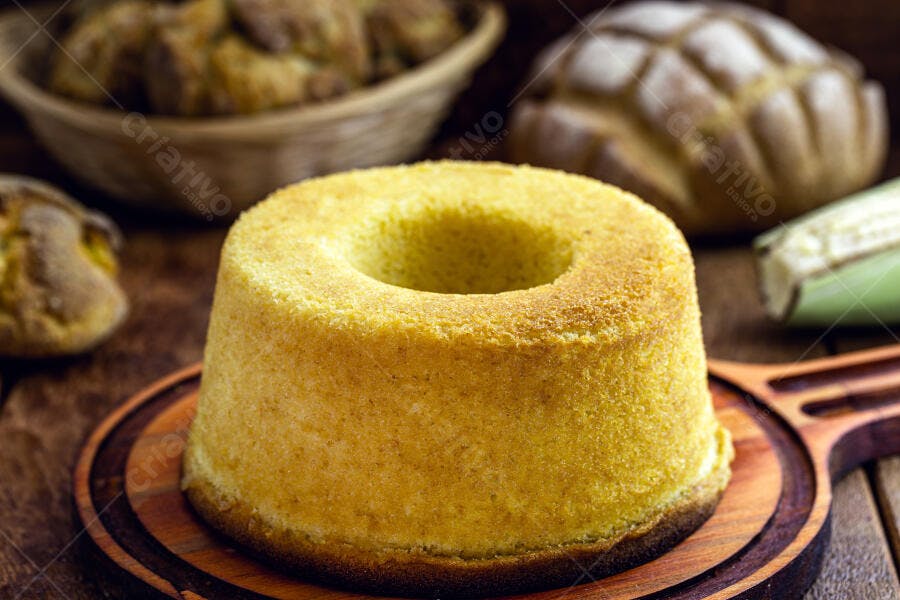 Bolo de fubá cremoso em tábua de madeira rústica com milho ao fundo