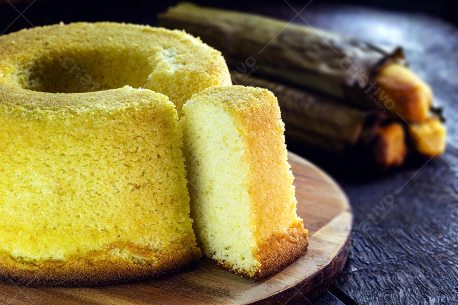 Bolo de fubá fatiado dourado em tábua de madeira rústica e milho no fundo
