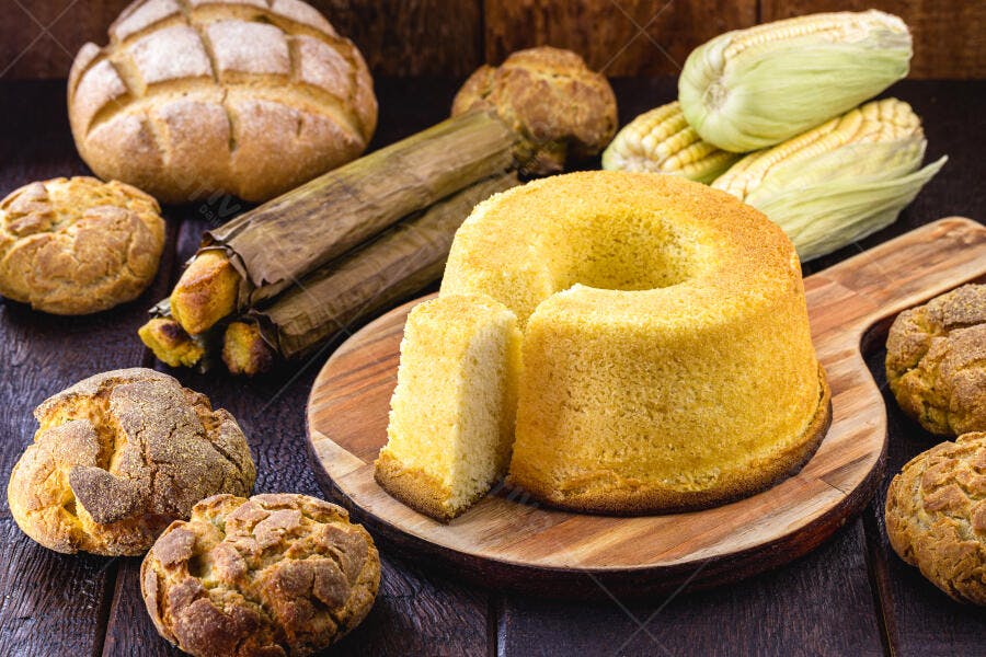 Bolo de milho pamonha e pães de fubá em mesa rústica de madeira