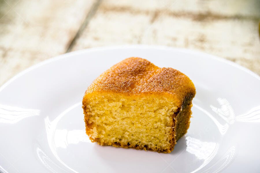 Fatia de bolo de milho dourado em prato branco sobre mesa rústica