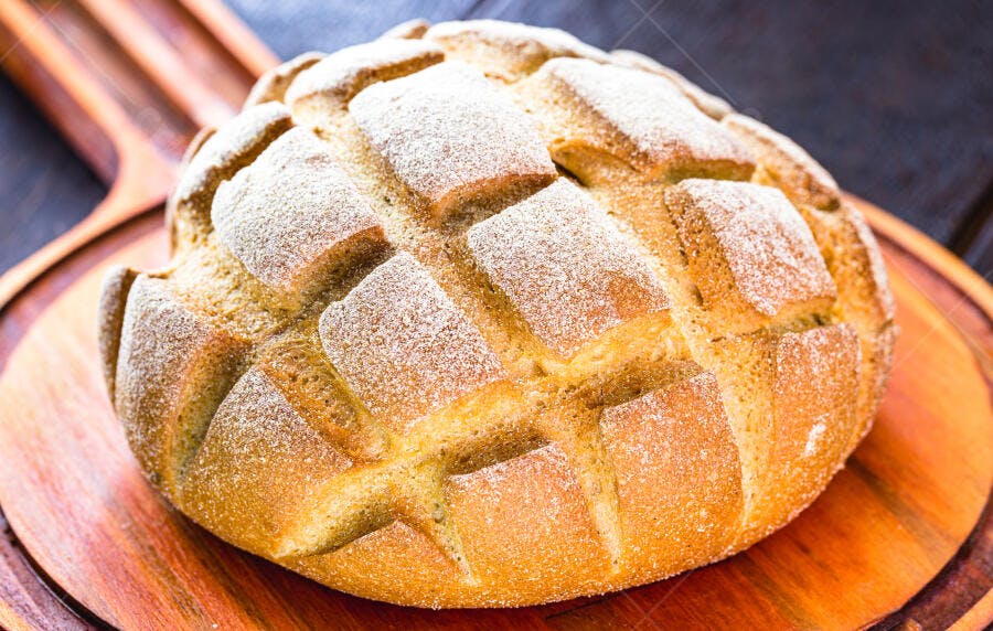 Pão artesanal rústico redondo com farinha sobre tábua de madeira