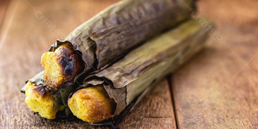 Pamonha tradicional amarela dourada embrulhada em folha de bananeira em mesa rústica