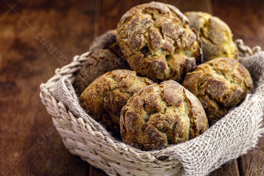 Pães rústicos variados em cesta de palha sobre mesa de madeira