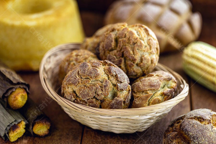 Pães de milho rústicos em cesta com bolo de fubá e pamonha em mesa de madeira