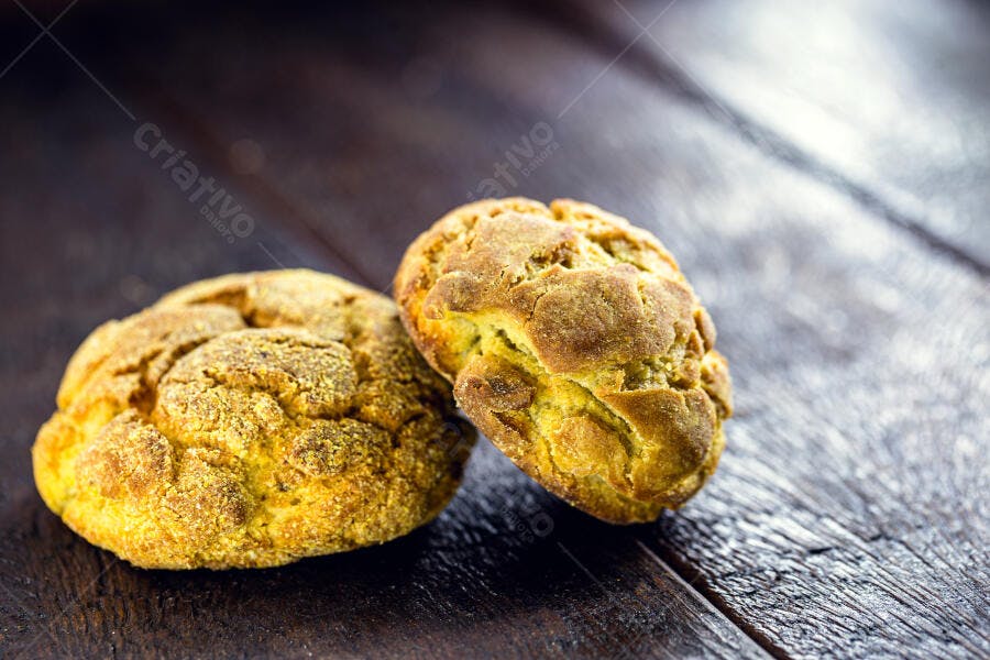 Pães de fubá rústicos dourados sobre mesa de madeira escura
