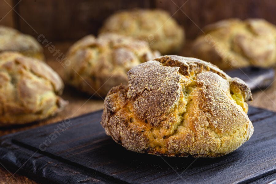Pão de milho artesanal dourado e crocante em tábua de madeira escura