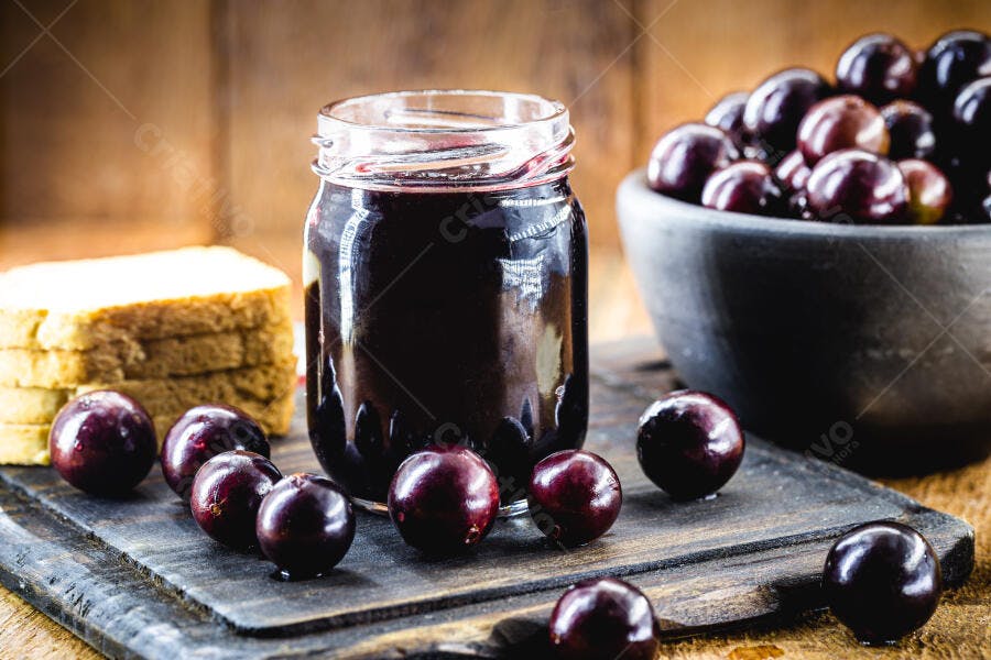 Geleia de jabuticaba caseira com frutas e pão em tábua rústica