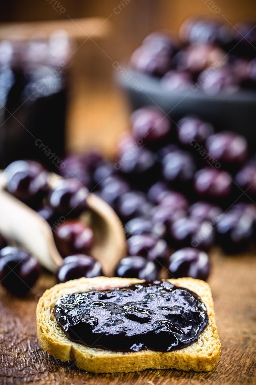 Torrada com geleia de frutas roxas sobre madeira rústica e frutas desfocadas