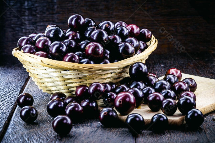 Jabuticabas frescas em cesto de vime e madeira rústica com frutas espalhadas