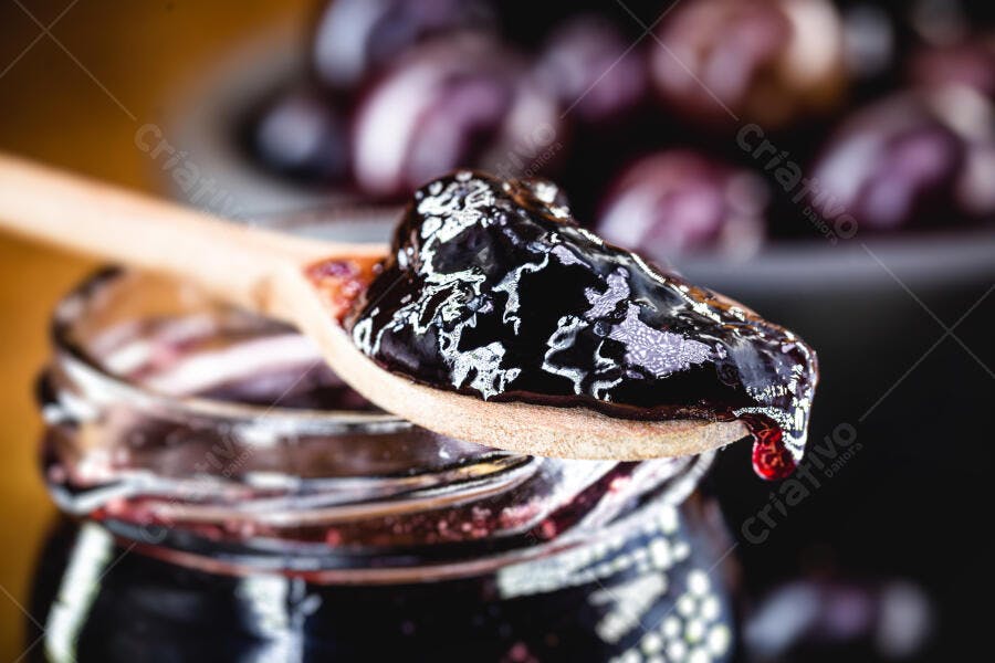 Geleia de frutas escuras roxa em colher de madeira sobre pote de vidro