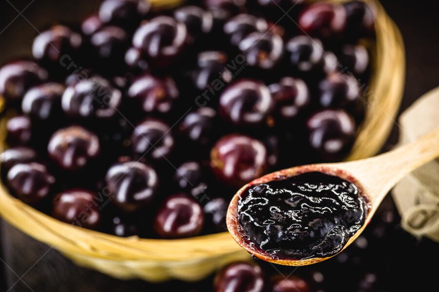 Jabuticabas frescas e geleia escura de fruta em colher de madeira