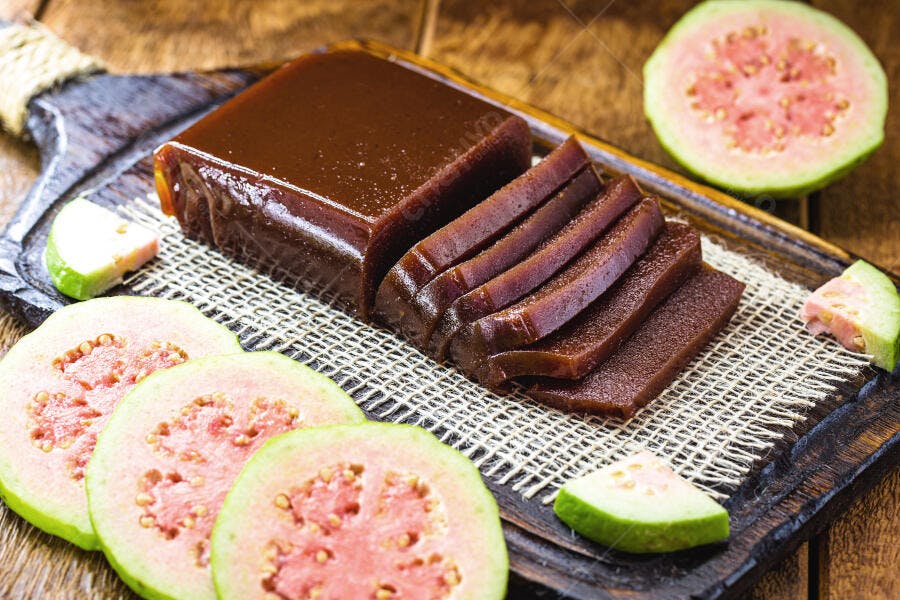 Goiabada fatiada com goiabas frescas rosadas em tábua de madeira rústica