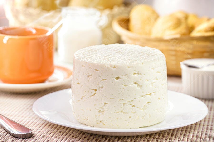 Queijo fresco branco em mesa de café da manhã com leite e pães