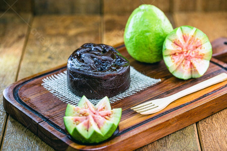 Goiabada escura com goiabas frescas verdes e rosadas em tábua de madeira