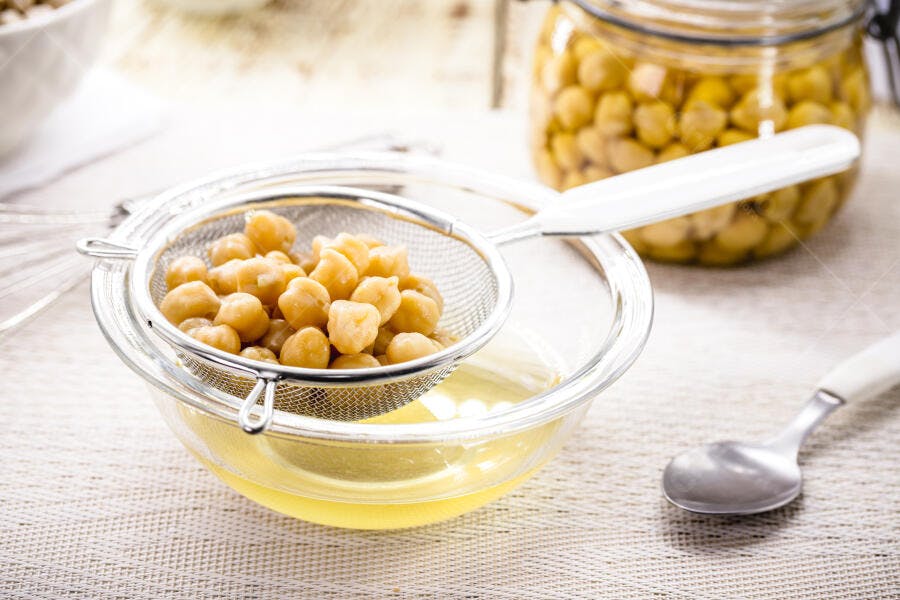 Grão de bico escorrido em peneira sobre tigela com aquafaba clara
