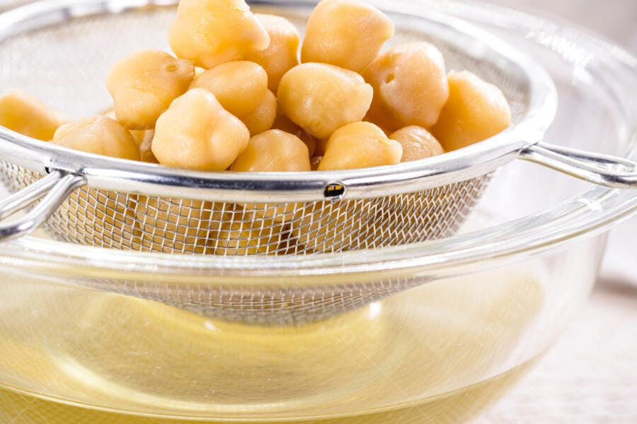 Grão de bico cozido drenando em peneira metálica para aquafaba
