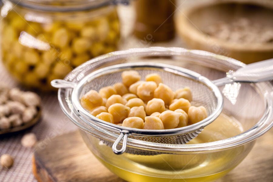 Grão-de-bico amarelo claro sendo escorrido em peneira com aquafaba