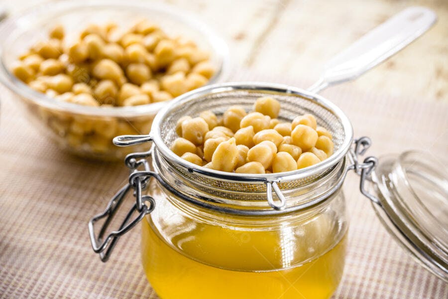Grão de bico cozido amarelo escorrendo em peneira sobre pote de aquafaba