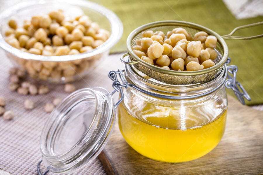 Grão de bico cozido e aquafaba dourada em potes de vidro na cozinha