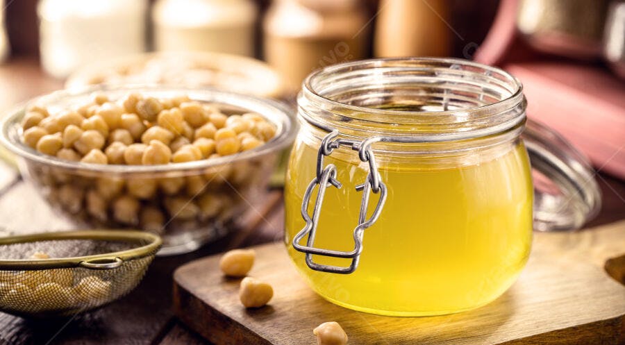 Aquafaba em pote de vidro com grão de bico cozido e peneira metálica