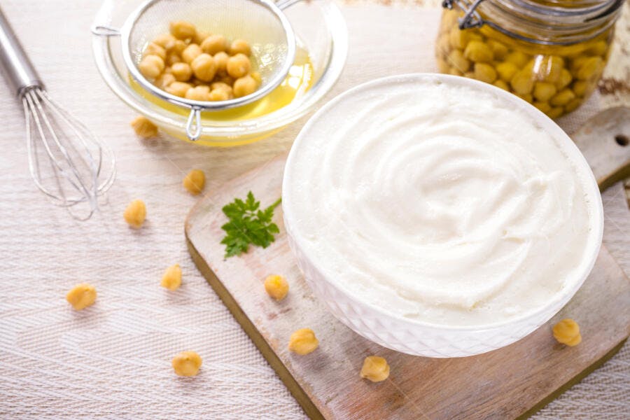 Aquafaba vegana em tigela branca com grão de bico e batedor de cozinha