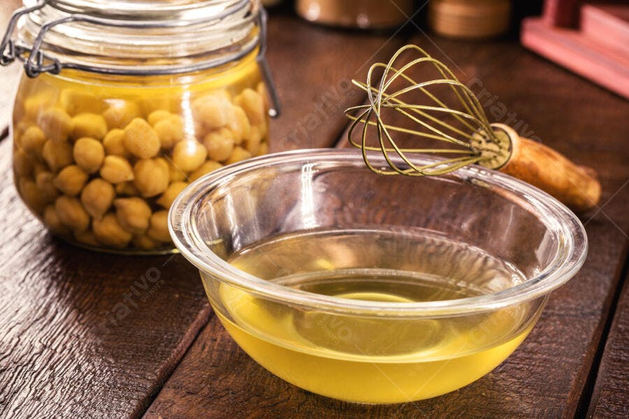 Grão de bico e aquafaba em potes de vidro com batedor de arame em cozinha rústica