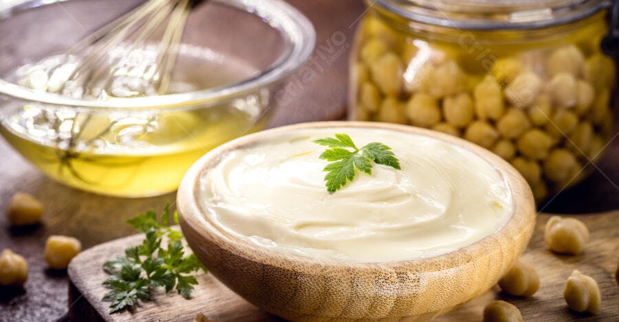 Maionese vegana de grão de bico em tigela de madeira com salsinha e azeite