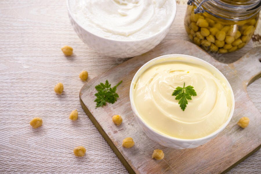 Tigelas de homus e molho cremoso amarelo com grão de bico e salsa em tábua de madeira