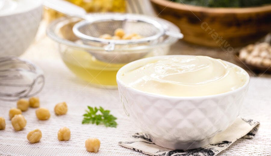 Maionese vegana cremosa em tigela branca com grão de bico e aquafaba