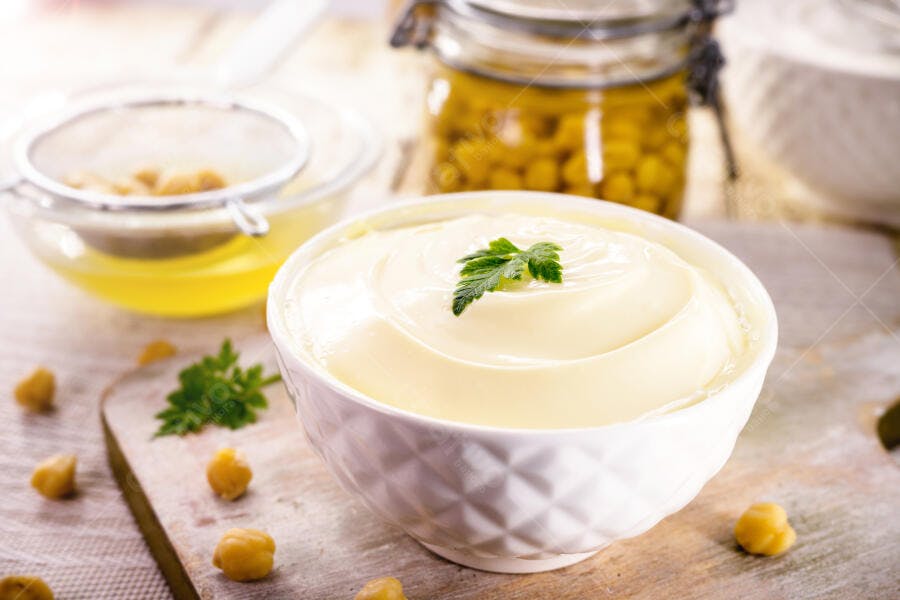 Maionese de aquafaba vegana amarela clara em tigela branca com grão de bico e salsa fresca