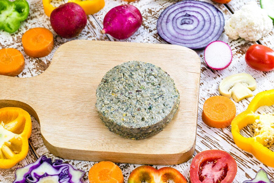 Hambúrguer vegano verde com vegetais frescos coloridos em tábua de corte