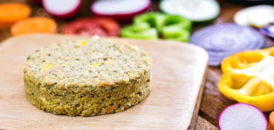 Hambúrguer vegetariano verde em tábua de madeira com legumes frescos coloridos