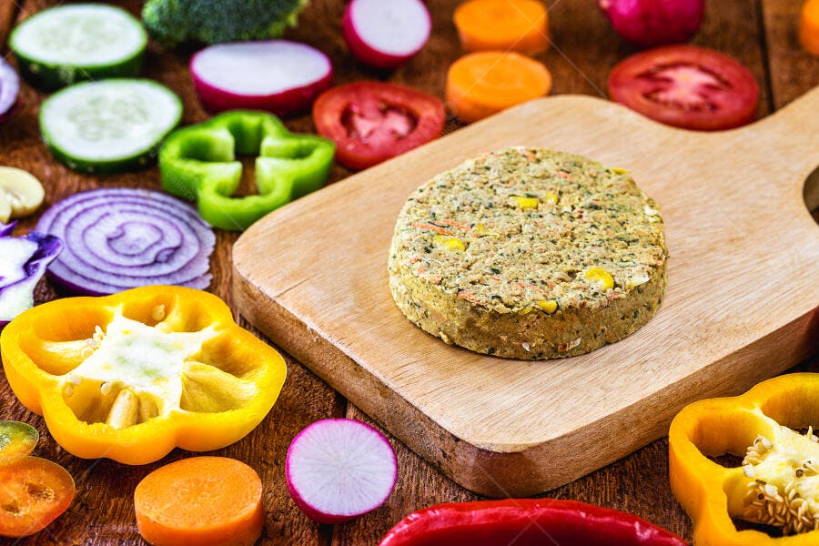 Hambúrguer vegano em tábua de madeira com vegetais frescos coloridos